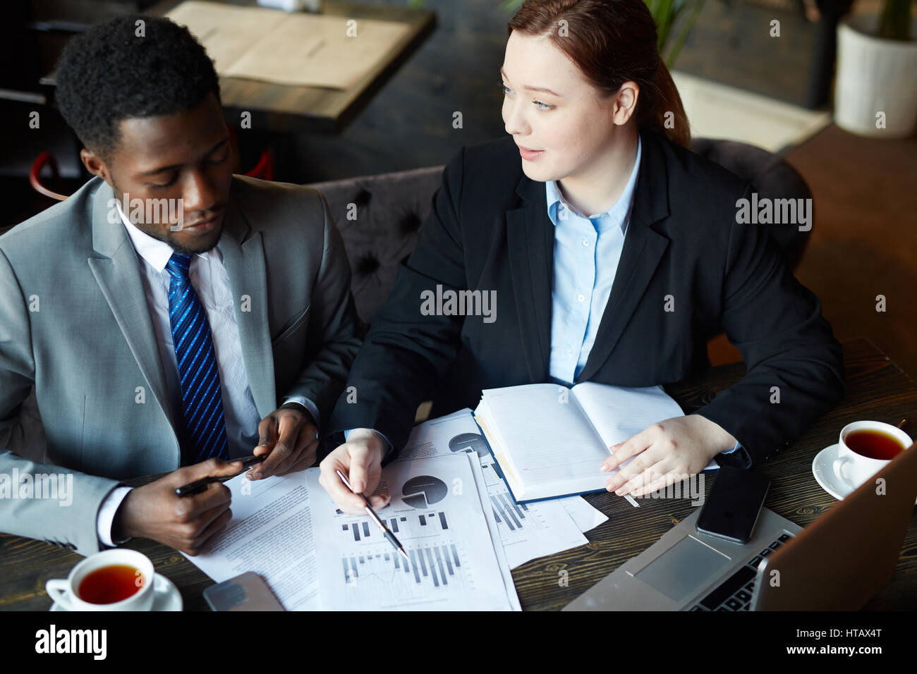 Ritratto di due uomini di affari che incontro in moderno Cafe: giovane donna professionale rivolta alle statistiche grafici mentre spiegare i dati a un collega Foto Stock