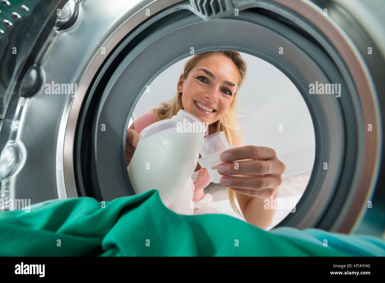 Giovane donna sorridente versando detergente in un coperchio dall'interno della macchina di lavaggio Foto Stock