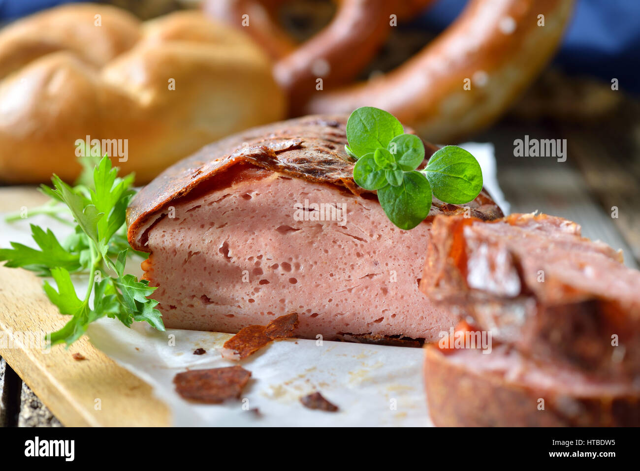 Forno tradizionale fresca bavarese pagnotta di carne con un marrone crosta croccante su un tagliere di legno guarnite con prezzemolo e origano, un rullo e un pretzel Foto Stock