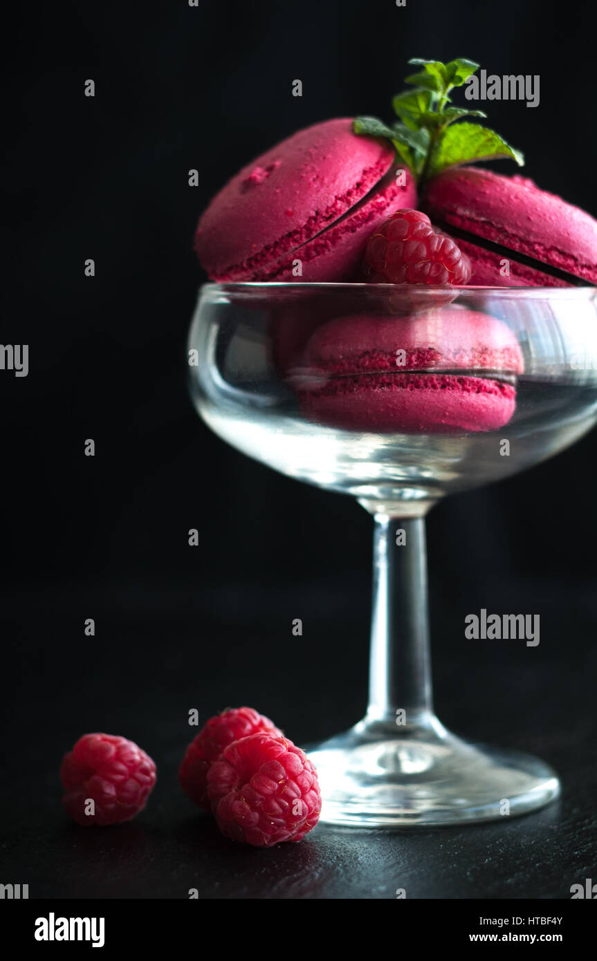 Amaretti rosa con lamponi in coppa su sfondo nero Foto Stock