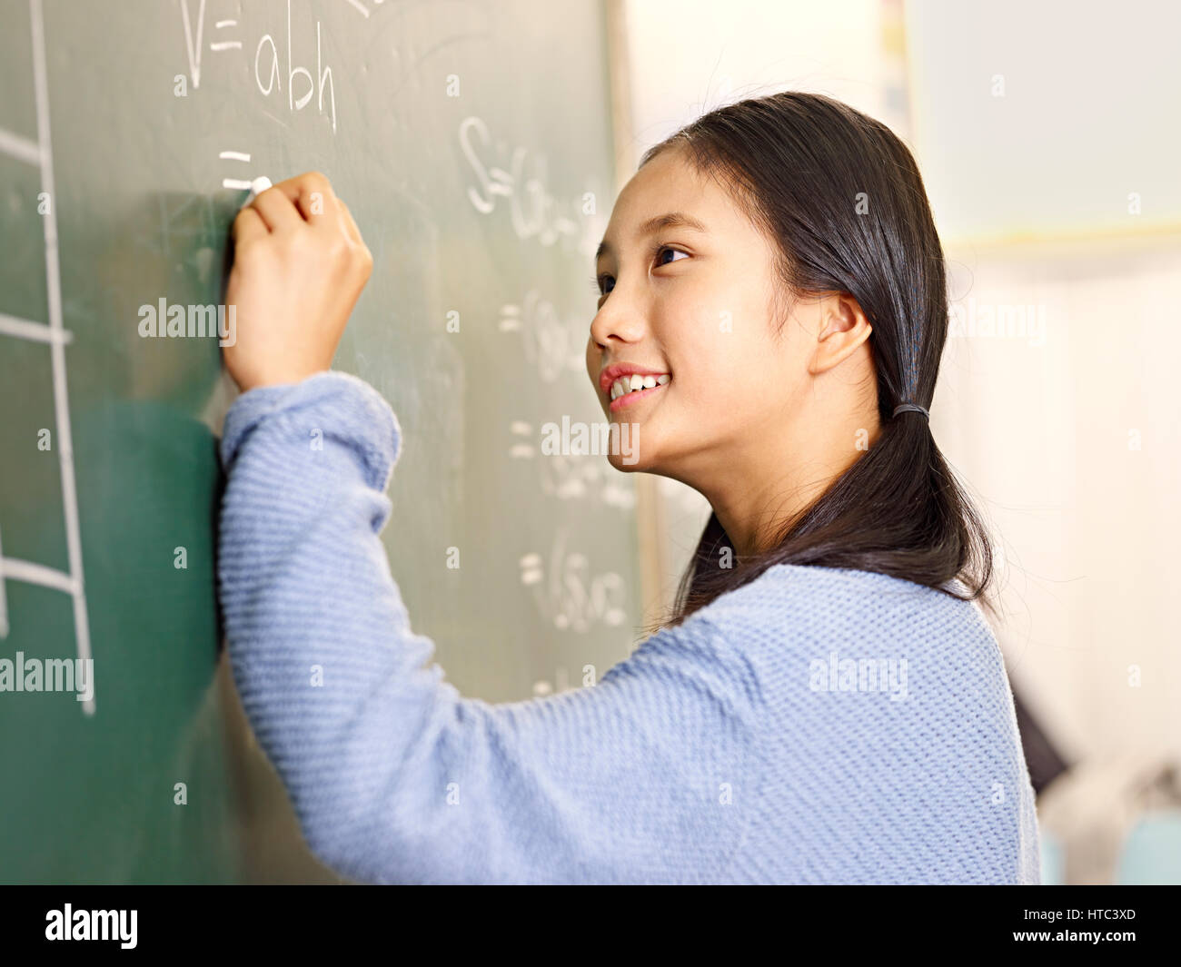 Fiducioso asiatici scuola elementare studente che scrive la risposta a un problema di geometria sulla lavagna. Foto Stock