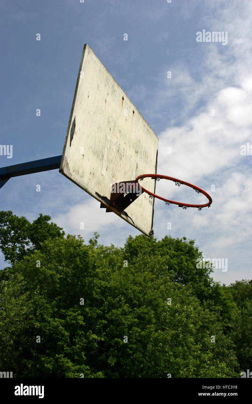 Basketball hoop con tavola spinale ma manca il net. Alberi e cielo blu con la nuvola bianca in background. Foto Stock