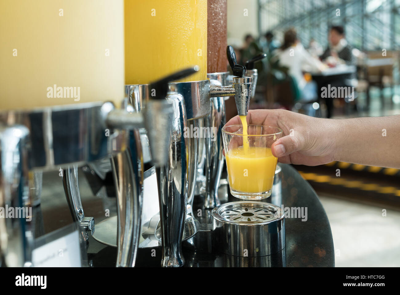 Mano azienda ricarica in vetro di succo d'arancia per la riga di succo di frutta fresco presso il ristorante a buffet, succhi di frutta a buffet self service nella mattina presso l'hotel. Foto Stock