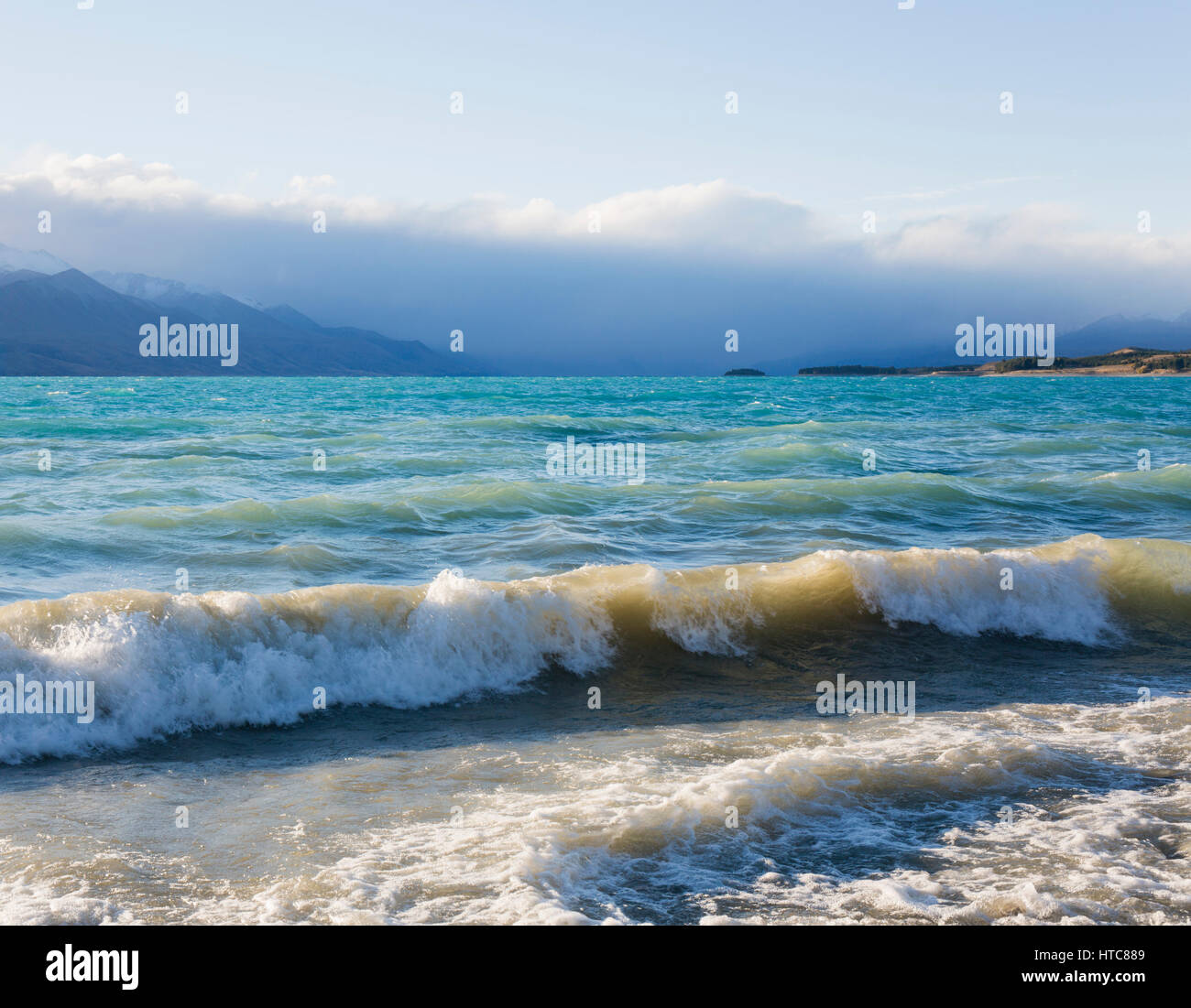 Twizel, Canterbury, Nuova Zelanda. Vista dalla riva attraverso le tempestose acque turchesi del Lago Pukaki, le Alpi del Sud oscurato dal cloud. Foto Stock