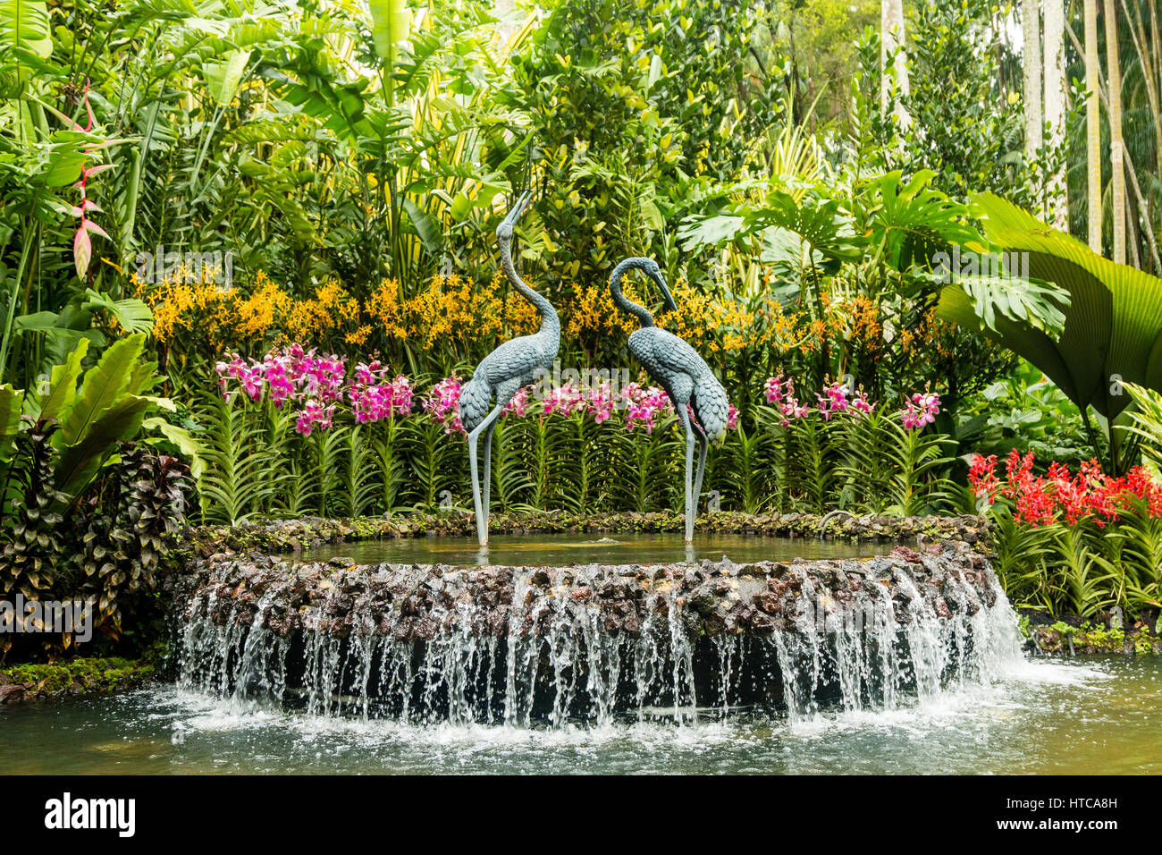 Elegante scultura di gru in una fontana a cascata circondata da splendide orchidee nel giardino di orchidee, Singapore Botanic Gardens, Asia Foto Stock