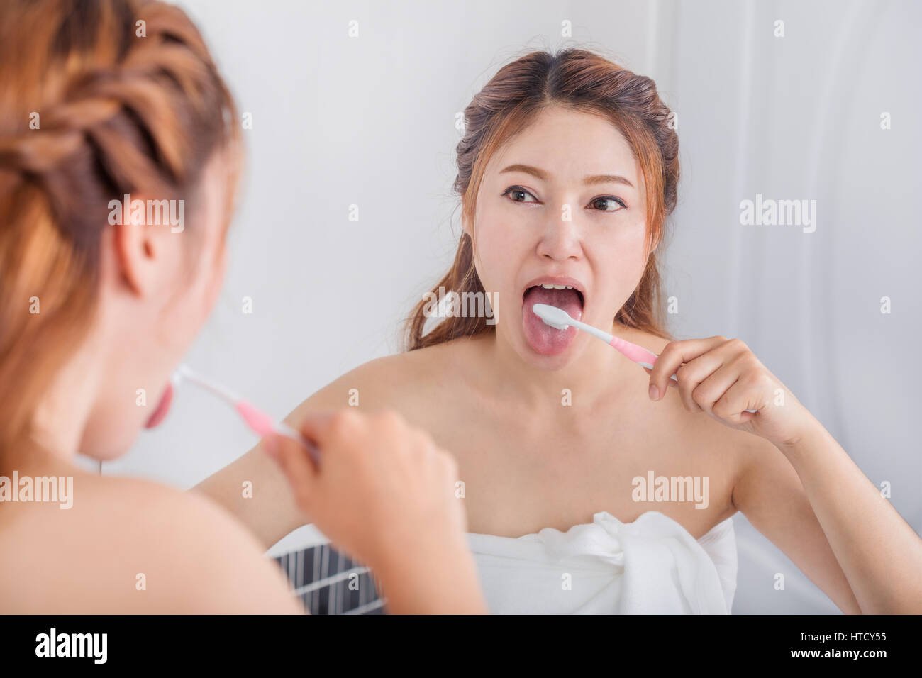 Donna linguetta di pulizia utilizzando uno spazzolino da denti con specchio del bagno Foto Stock