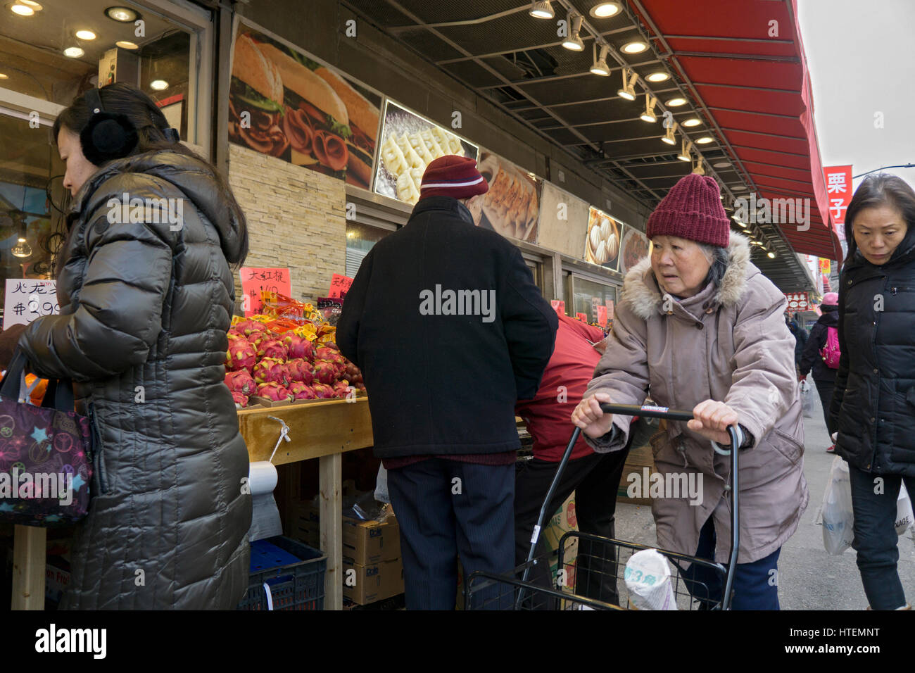 Un vecchio cinese donna americana spingendo un carrello in prossimità di una frutta stand in CHinatown, lavaggio, Queens, a New York City. Foto Stock