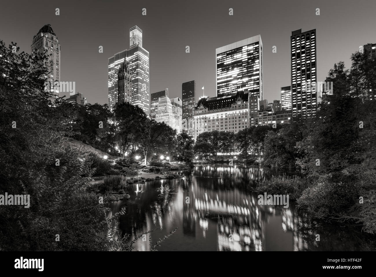 Midtown Manhattan grattacieli illuminati in serata.Gli edifici di Central Park South sono riflessa nello stagno. La città di New York. Bianco & nero Foto Stock