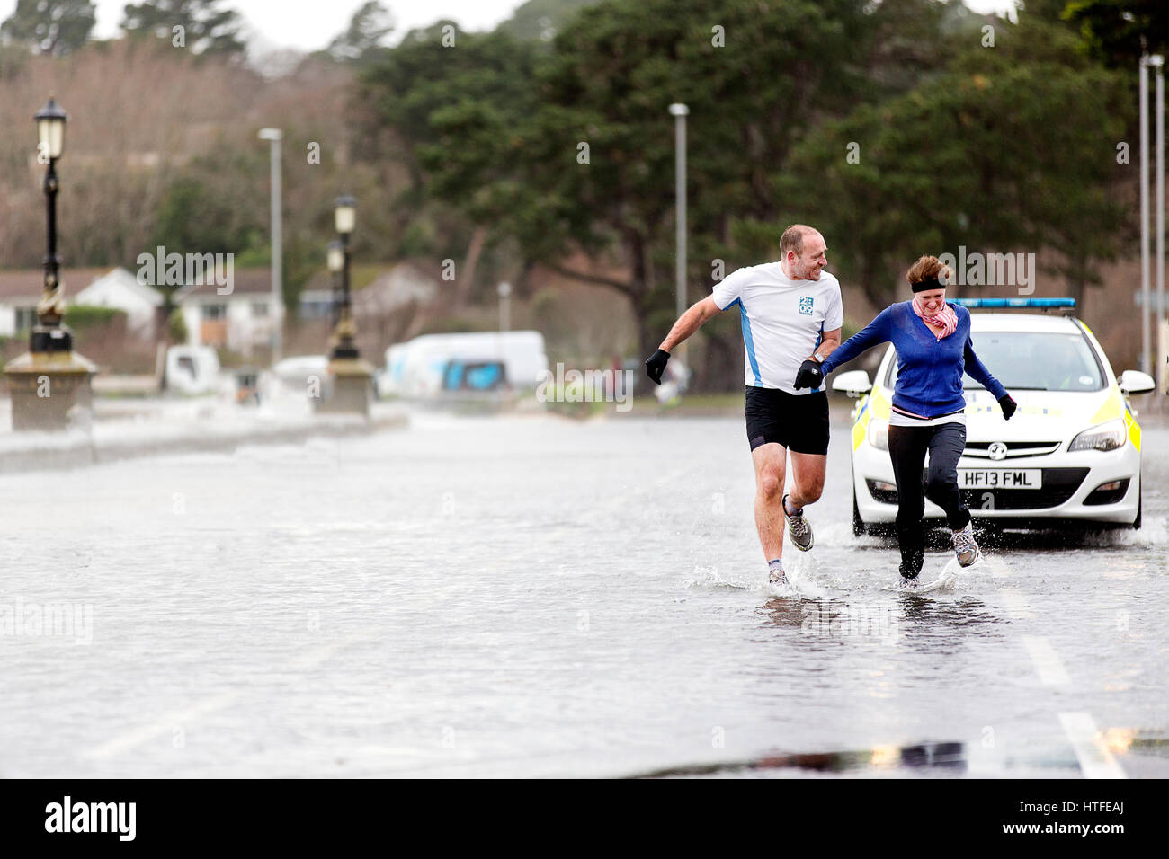 Una coppia maschile e femminile non scoraggiata che fa jogging attraverso pozze d'acqua tempesta a Poole, Dorset come Storm Eleanor batte la costa meridionale dell'Inghilterra Foto Stock