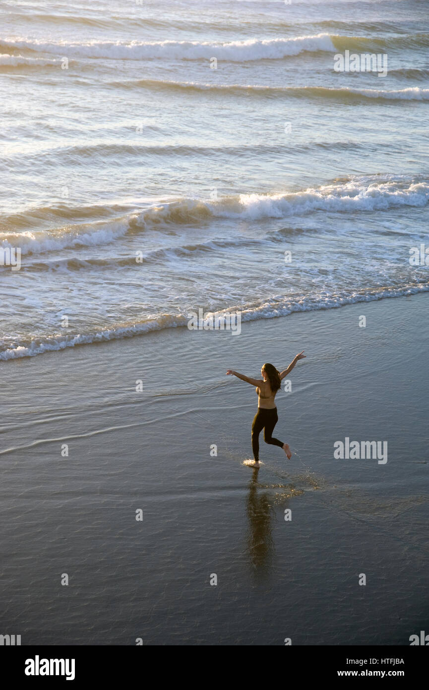 La donna in esecuzione nell'oceano vicino al molo presso la spiaggia di Venezia, CA Foto Stock