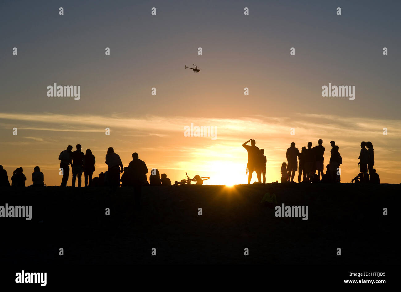 La gente a guardare il tramonto a Venice Beach in California come una guardia costiera elicottero vola in passato. Foto Stock