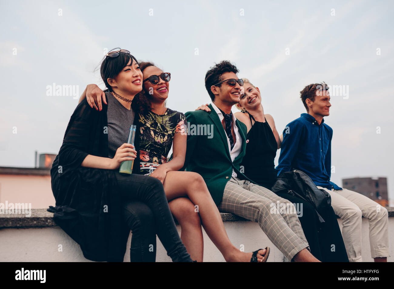 Colpo di giovani amici appendere fuori insieme sul tetto. Gruppo multirazziale di persone seduti sulla terrazza e godersi. Foto Stock