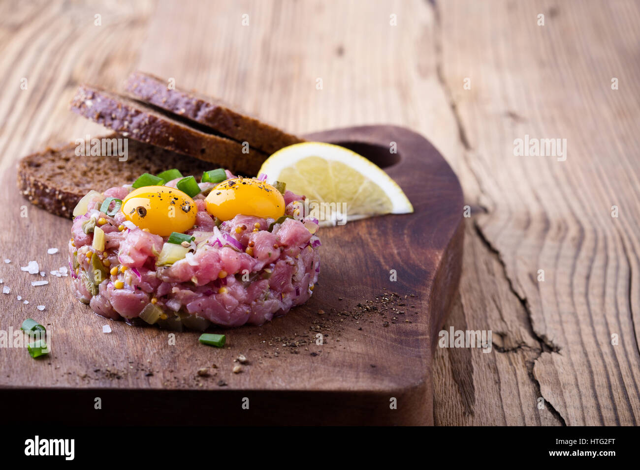 Tartare di manzo sagomato in stampo ad anello, guarnita con due uova di quaglia tuorli e servita con pane di segale sul tagliere di legno Foto Stock