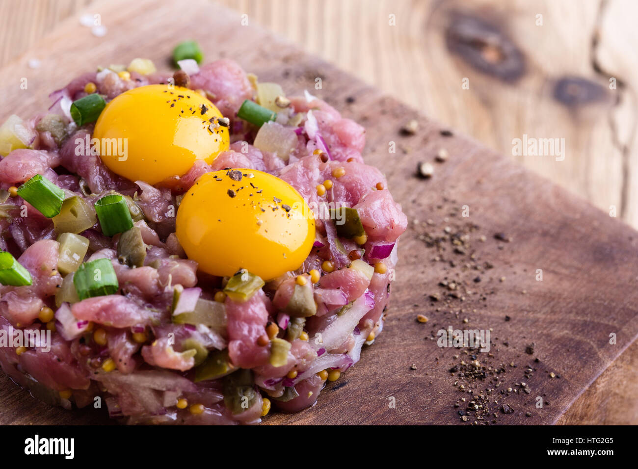 Tartare di manzo sagomato in stampo ad anello, guarnita con due uova di quaglia tuorli e servita con pane di segale sul tagliere di legno Foto Stock