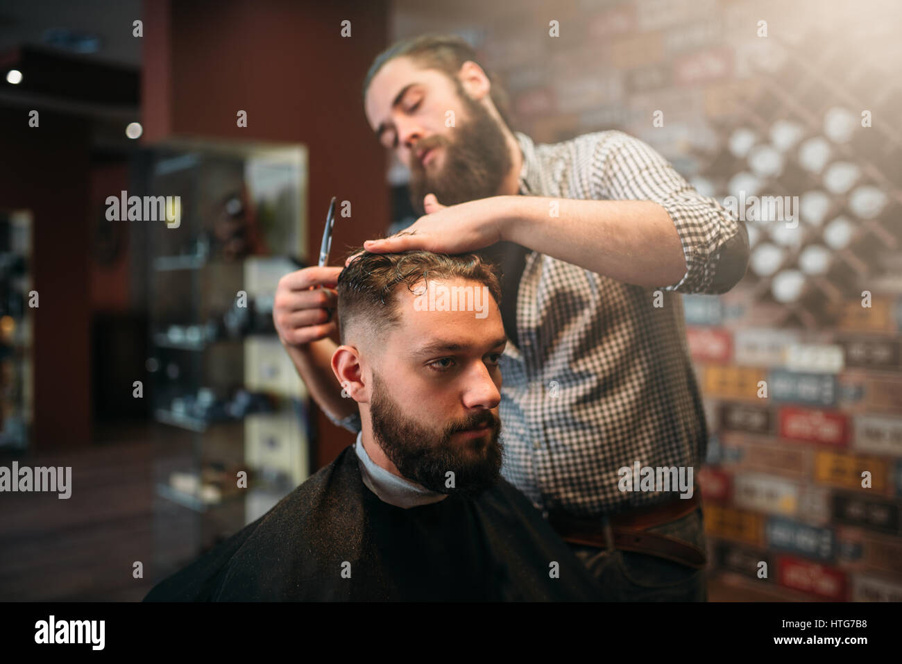 Coiffeur taglio a forbice dei capelli del cliente man in black salon cape, barbiere sullo sfondo Foto Stock