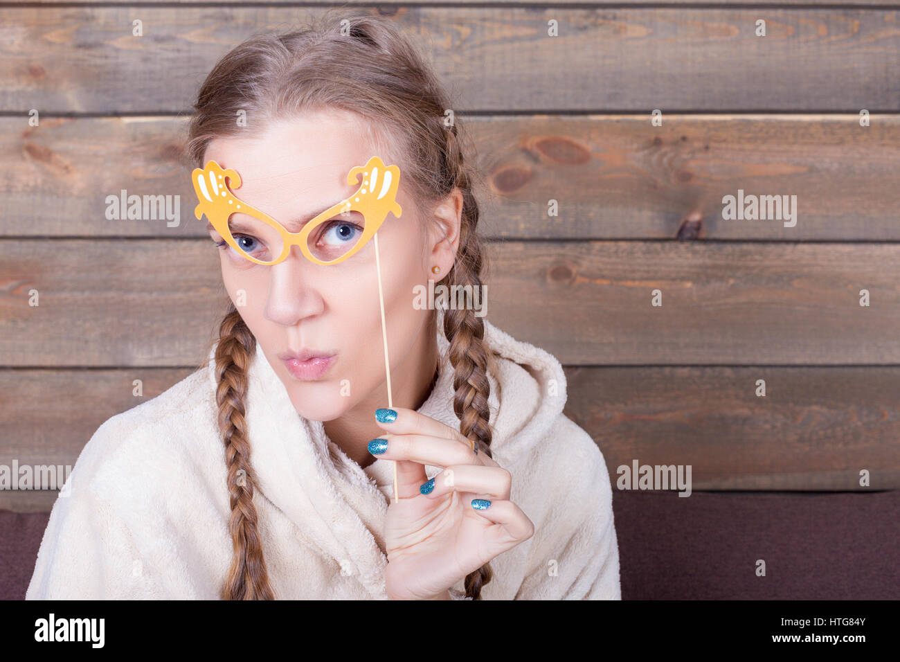 Giovane donna con gli occhiali giallo su un bastone, sullo sfondo di legno. Funny foto puntelli. Accessori divertenti per germogli Foto Stock