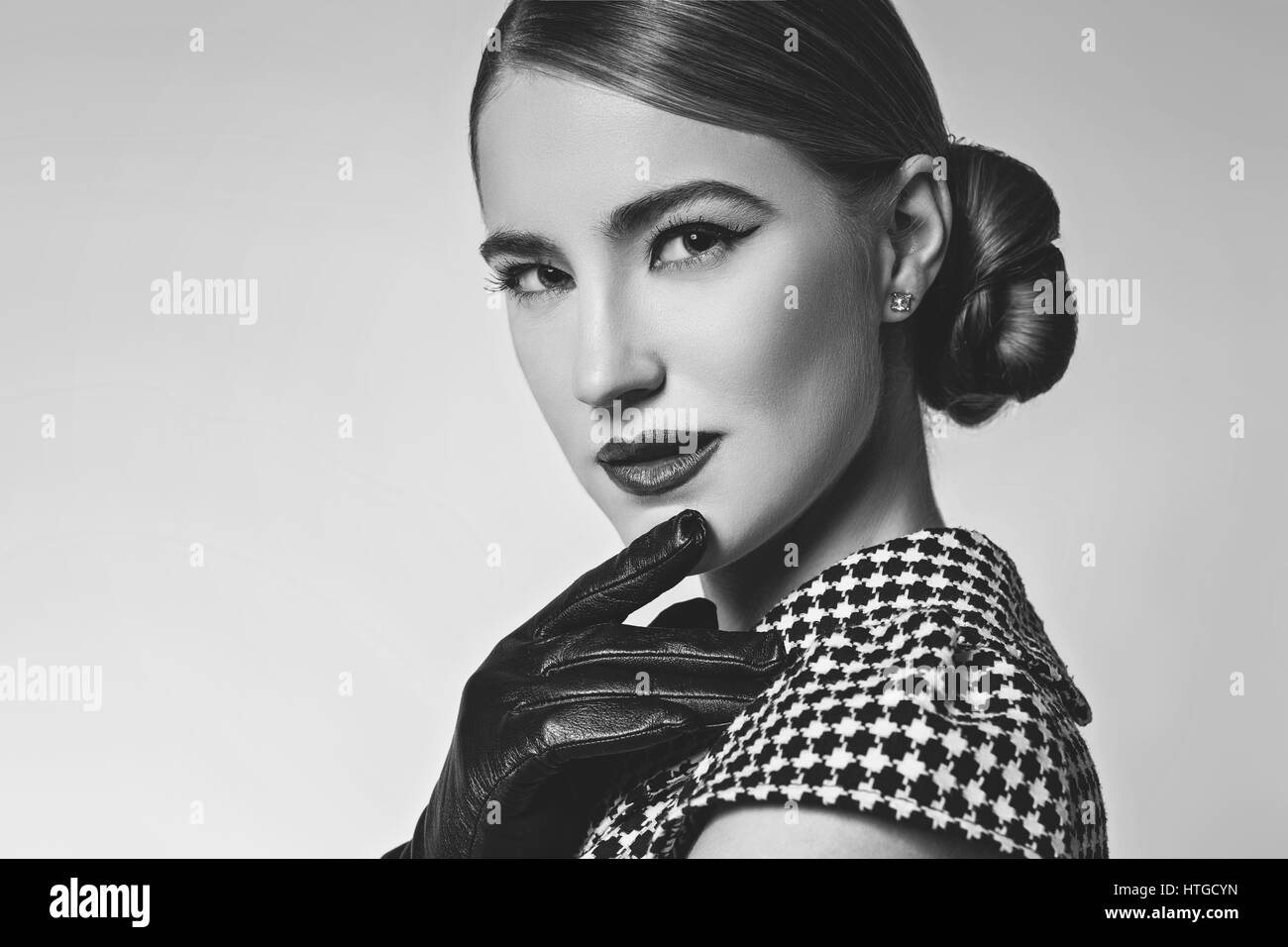 Bella giovane donna con labbra rosse per il make-up retrò in bianco e nero degli abiti e guanti in pelle in piedi su sfondo grigio. Monocromatico. Copia dello spazio. Foto Stock