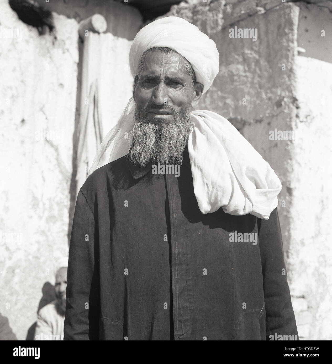 Ritratto di strada preso negli anni '50 da J Allan Cash di un sacerdote afghano che indossa la testa e la giacca di cotone, in piedi fuori, Kabul, Afghanistan. Foto Stock