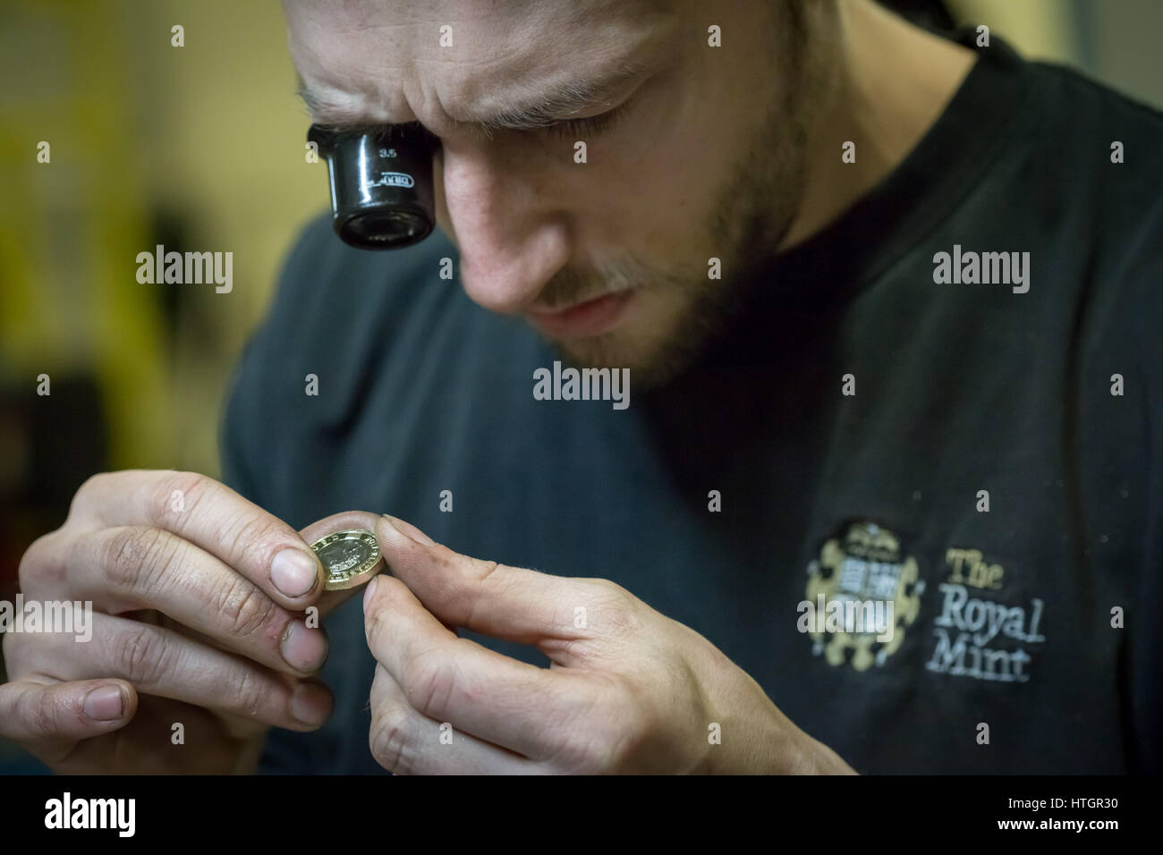 Llantrisant, nel Galles del Sud, Regno Unito. Il 14 marzo 2017. Byron West, 32, Coin Premere Setter. Egli ha lavorato per la Royal Mint per 4 anni. Egli controlla la qualità di uno appena premuto £1 moneta. © Guy Corbishley/Alamy Live News Foto Stock