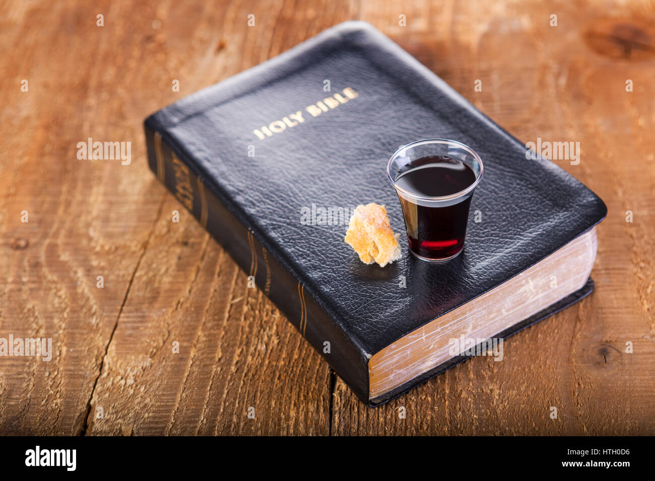 Tenendo la comunione. Bicchiere di vetro con il vino rosso, il pane e la Santa Bibbia sul tavolo di legno di close-up. La messa a fuoco su vetro Foto Stock