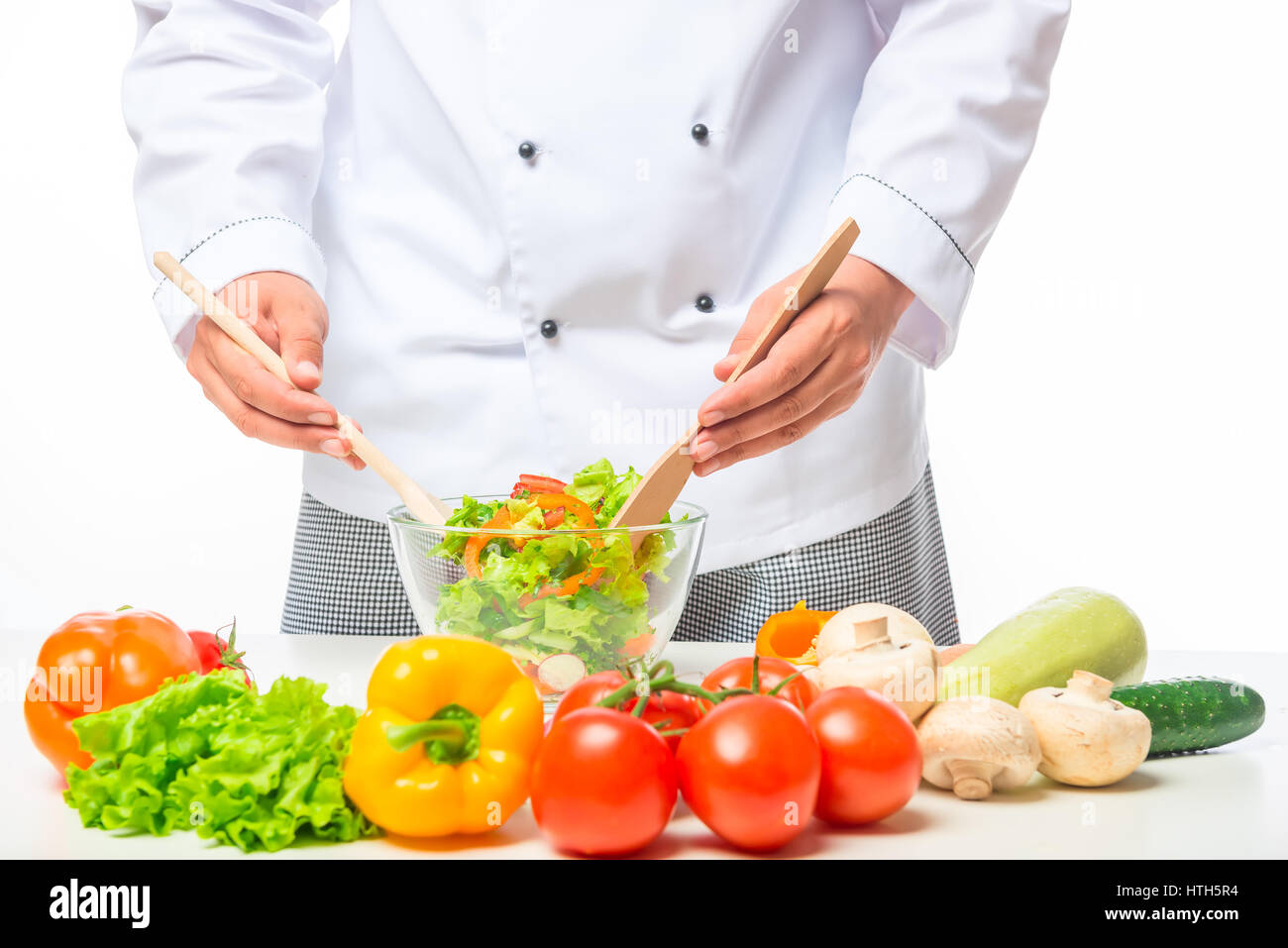 Mani chef mescolando con un cucchiaio di legno in insalata di verdure in una ciotola su un tavolo Foto Stock