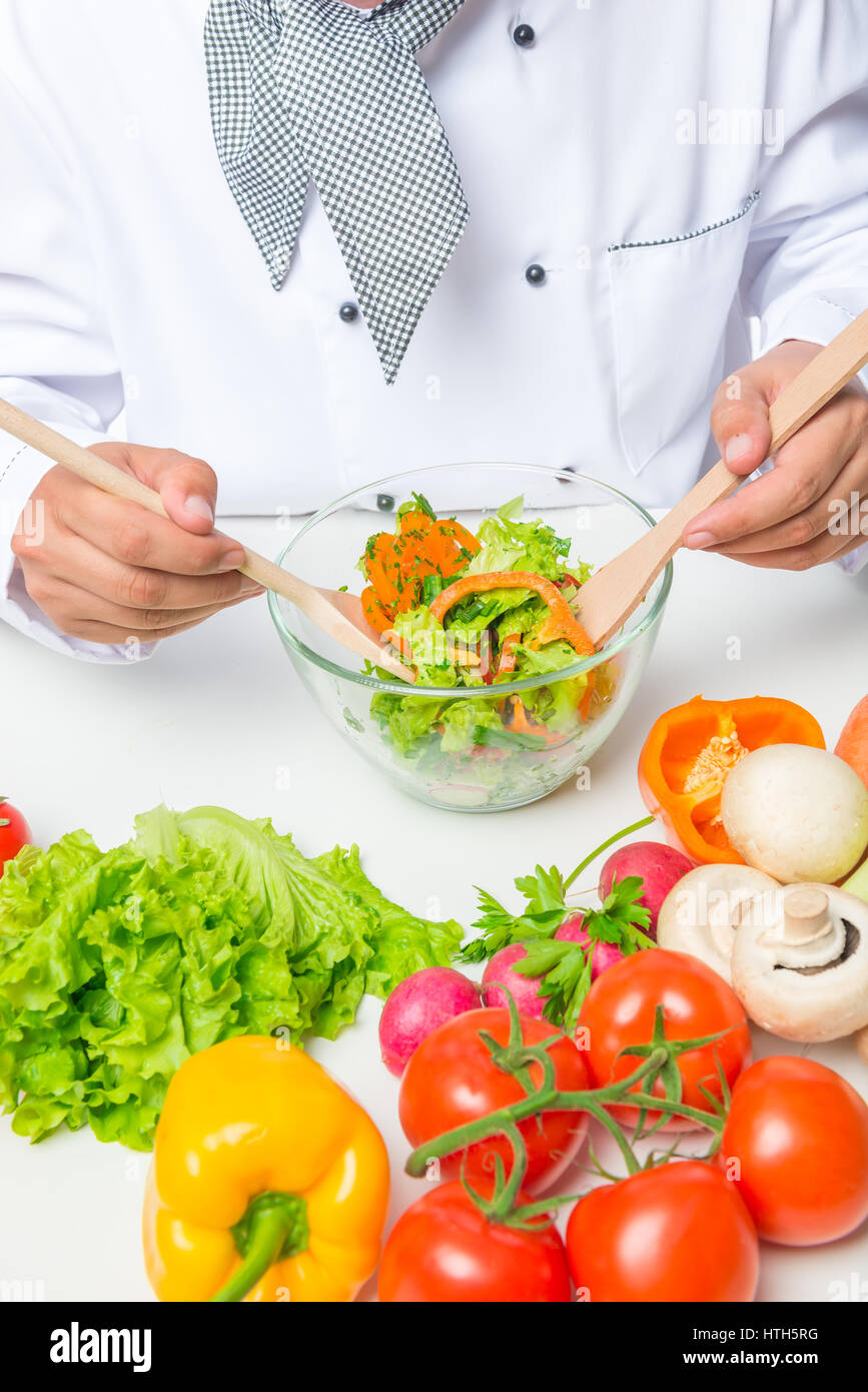 Cuocere le mani agitata di insalata di verdure con due cucchiai di legno su un tavolo bianco Foto Stock