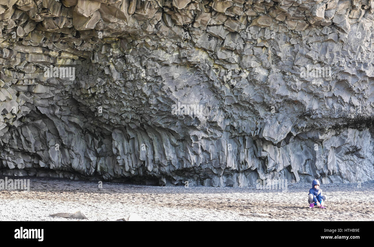 Un piccolo bambino sembra piccolo in confronto ad alta scogliera di basalto e grande caverna a Reynisfjara, Islanda, in inverno Foto Stock