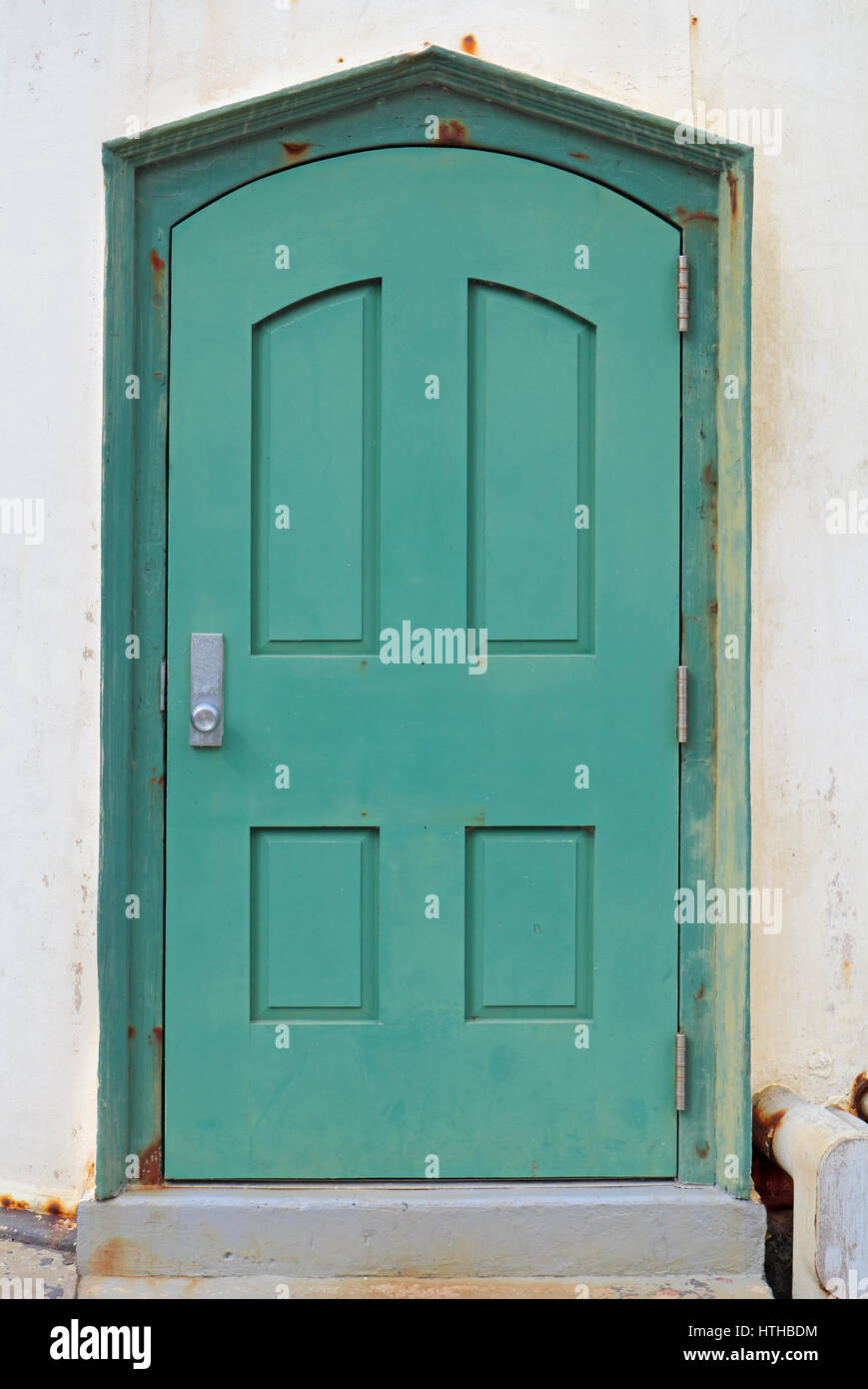 Vecchie e arrugginite, verde, metallo, porta ad arco in intonaco bianco muro di un edificio pubblico in California Foto Stock