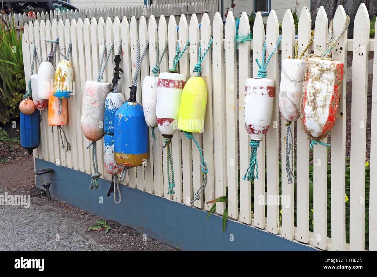 Diversi tipi e forme di marine boe pendente da un recinto di picchetti bianchi vicino alla costa della California Foto Stock