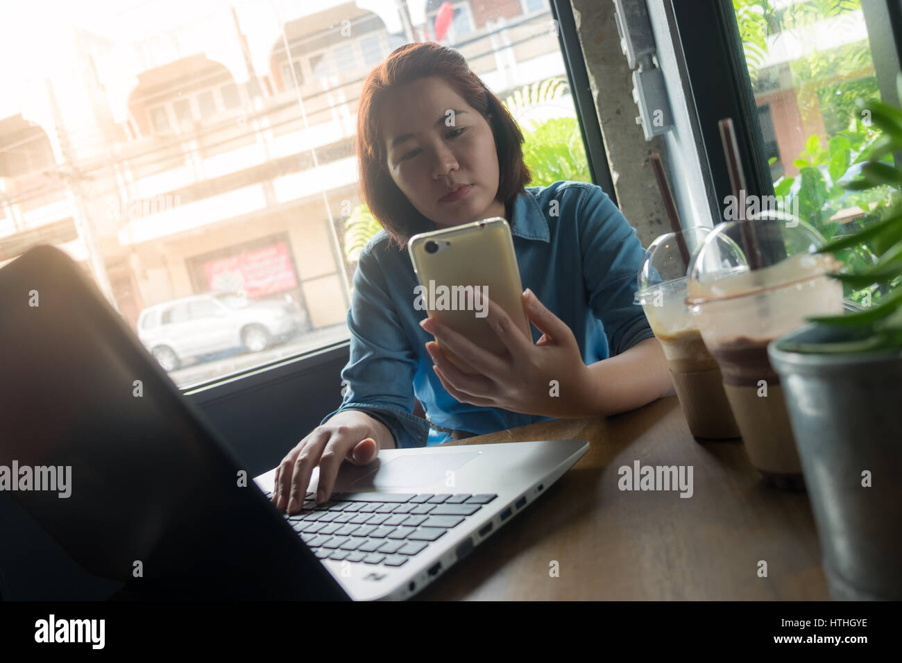 Giovane donna asiatica utilizza lo smartphone mentre si lavora in una caffetteria. Lavoratore Freelance sulla giornata lavorativa con il concetto di computer portatile Foto Stock
