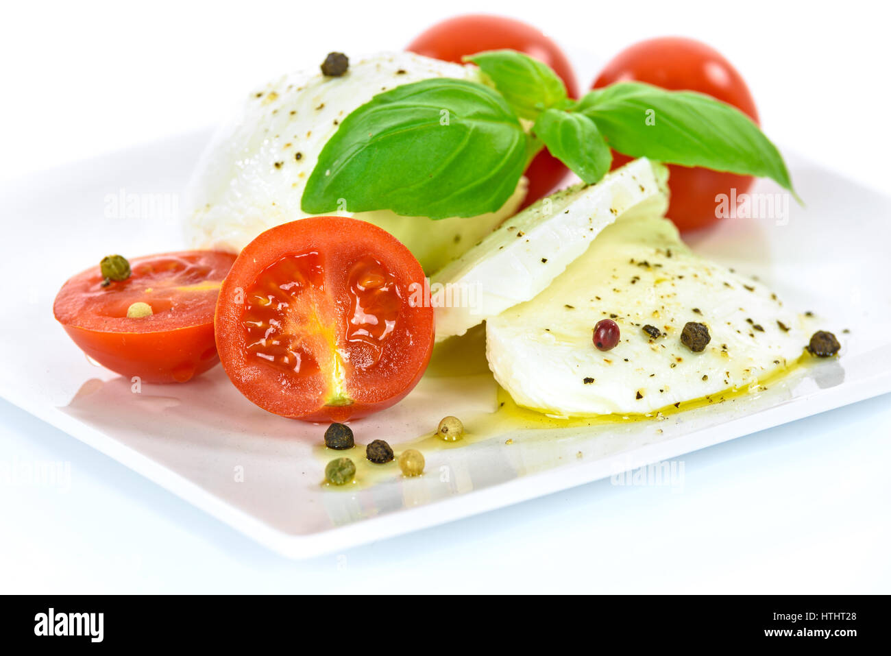 La delicatezza della cucina italiana - mozzarella con foglie di basilico e baby pomodori, condita con olio di oliva e pepe Foto Stock