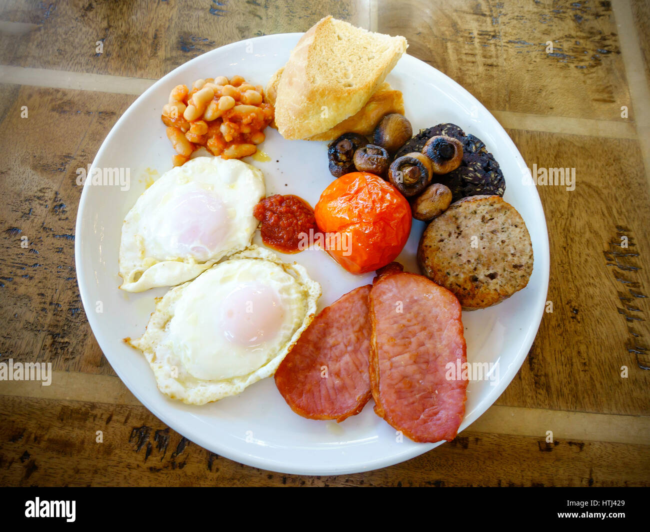 La completa prima colazione inglese due uova fritte, pancetta, fagioli al forno, pane bianco tostato, budino nero, pomodoro grigliate, salsiccia e ketchup Foto Stock