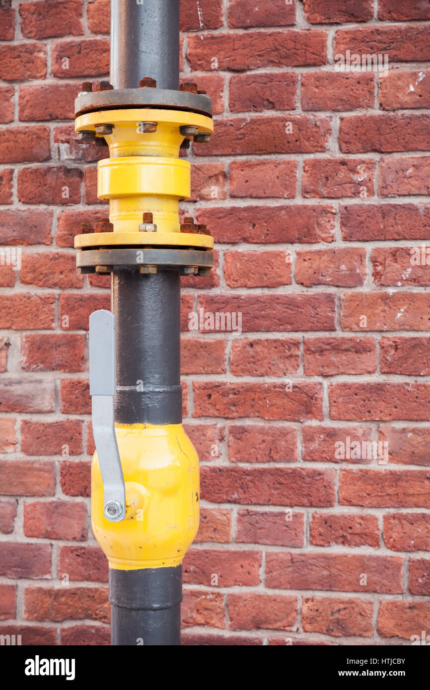 Tubo del gas con valvola aperta rosso sopra un muro di mattoni Foto Stock