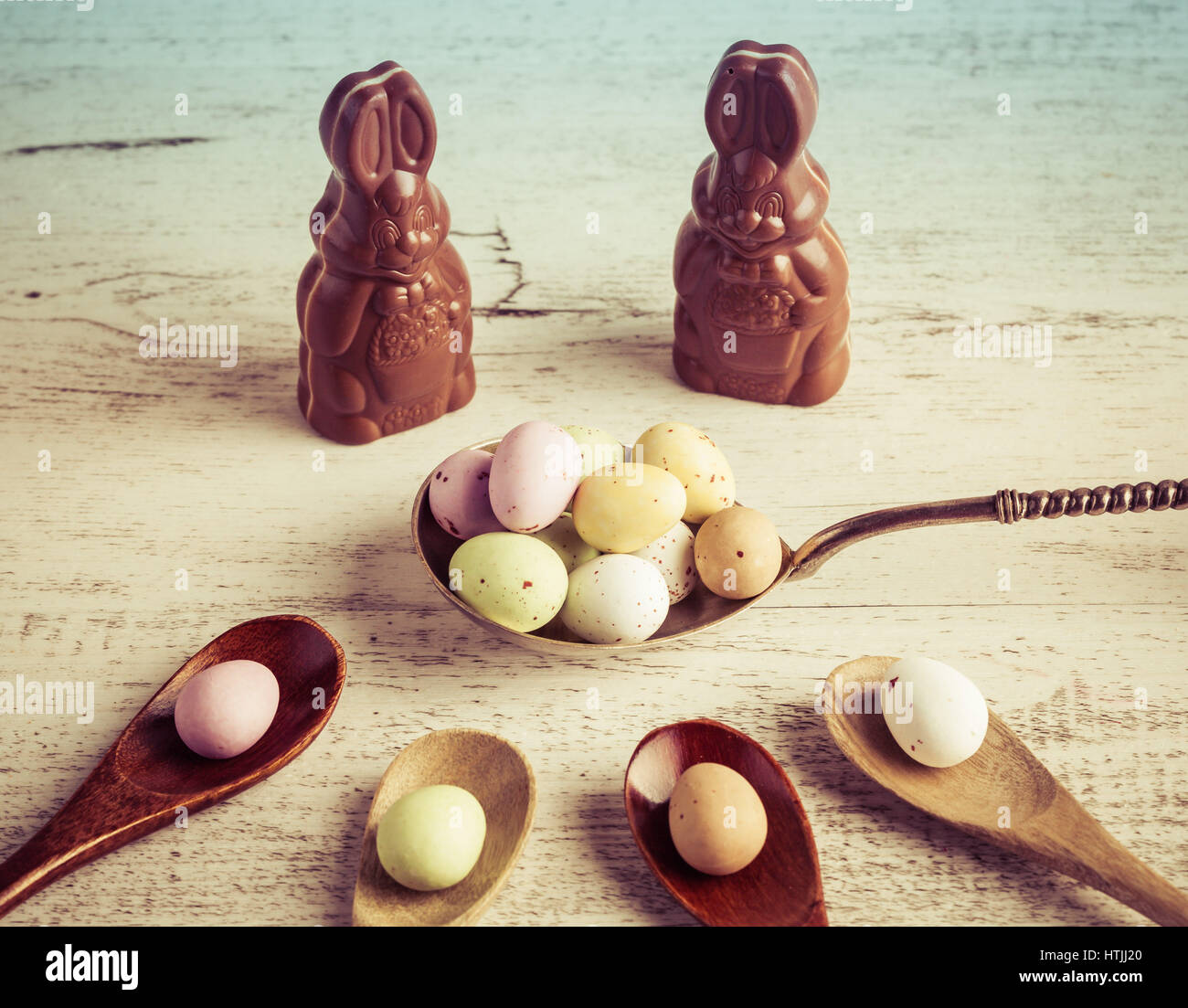 Pasqua rivestite di zucchero candito uova su legno e argento cucchiai con coniglietti di cioccolato bianco su sfondo di legno Foto Stock