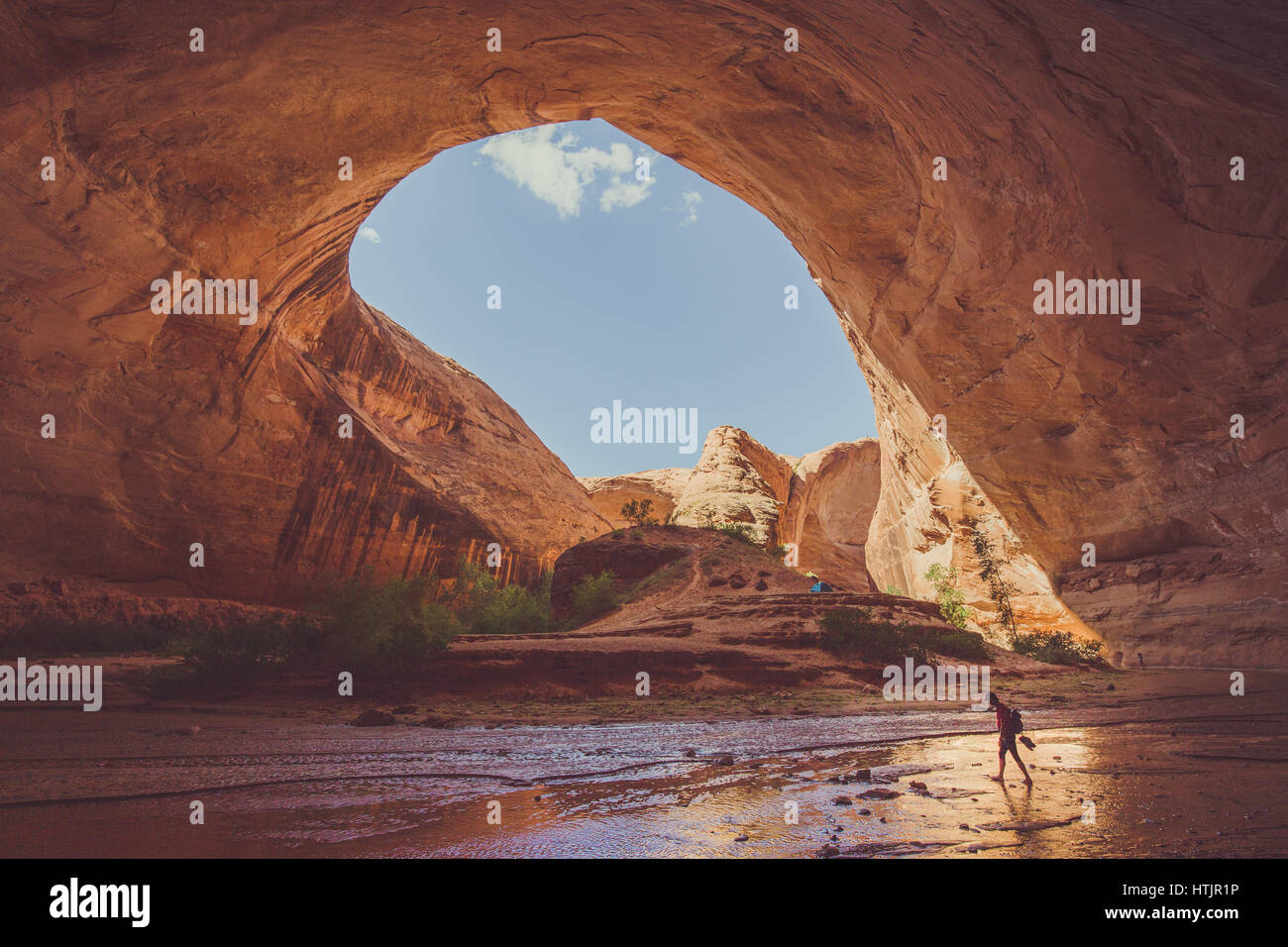 Ampio angolo di visione dei maschi di escursionista backpacking sotto splendide Jacob Hamblin Arch in Coyote Gulch in una giornata di sole con cielo blu e nuvole in estate, Utah Foto Stock