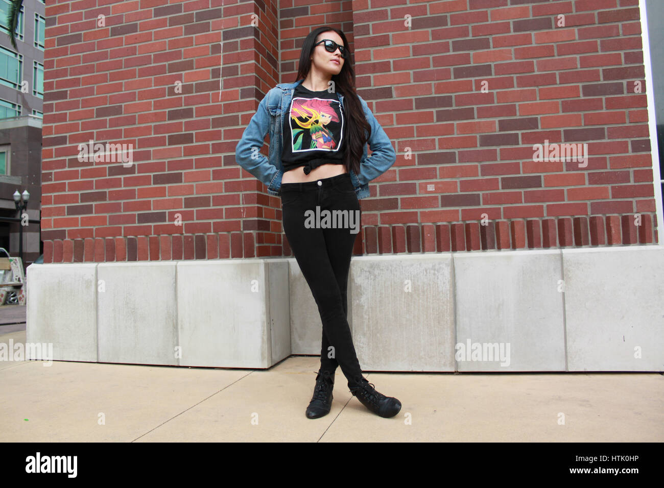 La modellazione femmina graphic t-shirt contro un muro di mattoni nel centro cittadino di Anaheim. Foto Stock