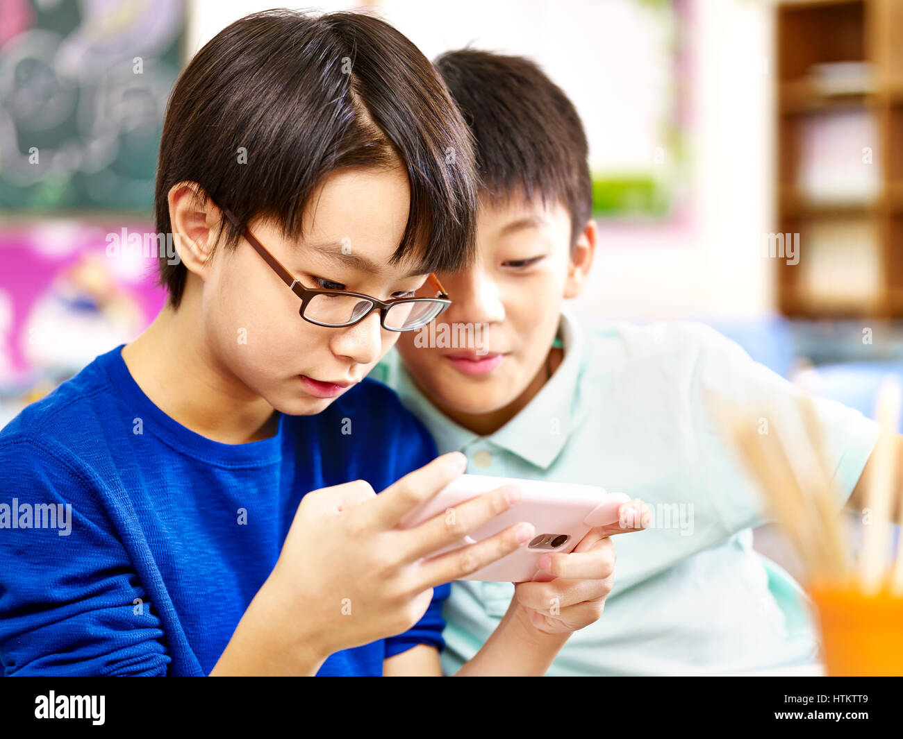 Due asian studenti della scuola primaria giocando online gioco utilizzando il telefono cellulare. Foto Stock