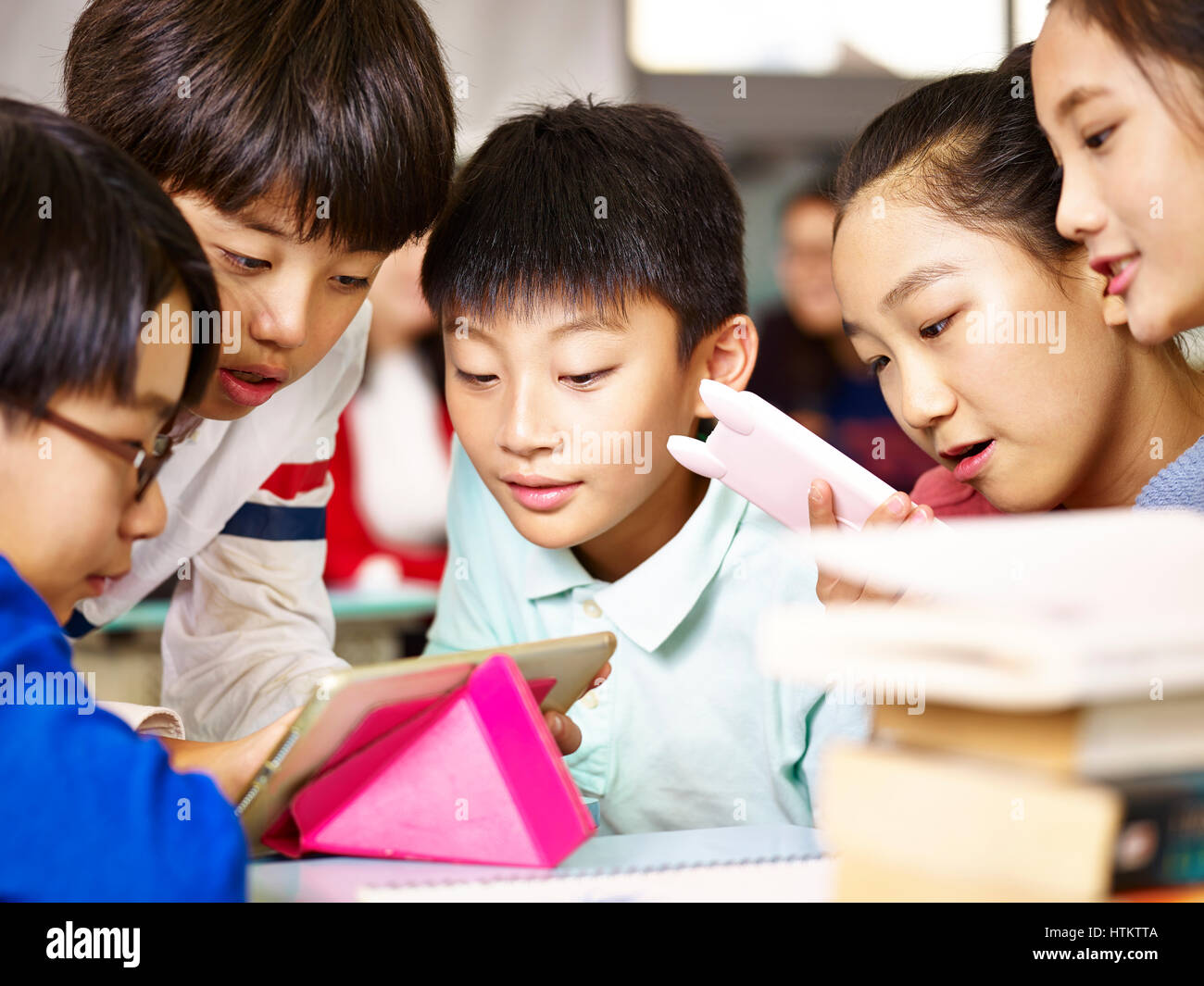 Gruppo di asiatici scuola elementare i bambini raccogliendo attorno a un gioco insieme usando il tablet durante la pausa. Foto Stock