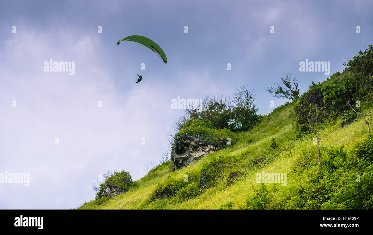 Parapendio volare le colline erbose sopra Gunung Payung Beach, Bali Foto Stock