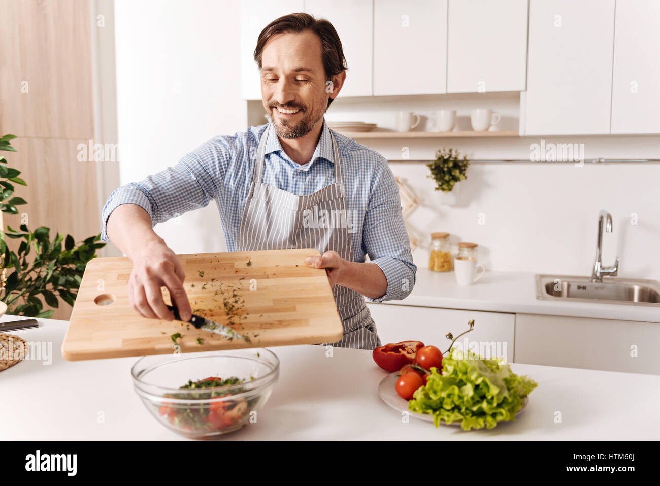 Soddisfatto uomo barbuto cucinare insalata di verdure a casa Foto Stock