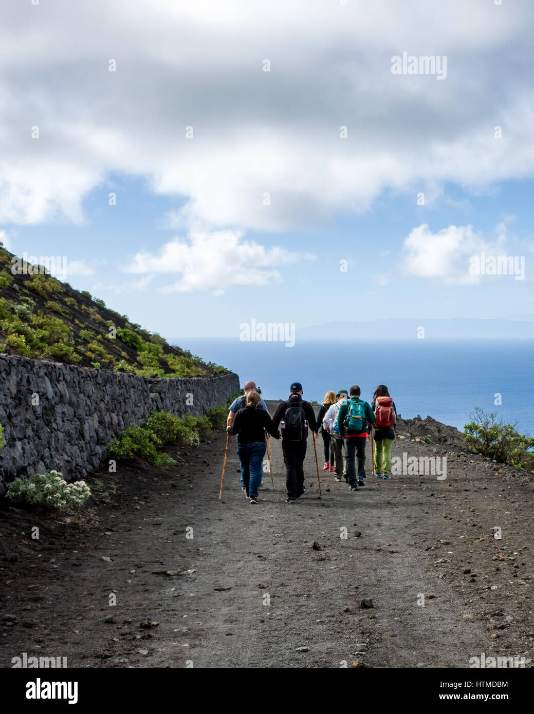 Sentiero escursionistico, Fuencaliente. La Palma. Tourist gli escursionisti a piedi lungo una strada di origine vulcanica sulla loro escursione guidata nella regione di Fuencaliente de la Palma. La vicina isola di Gomera è visibile all'orizzonte che guarda al mare. Foto Stock