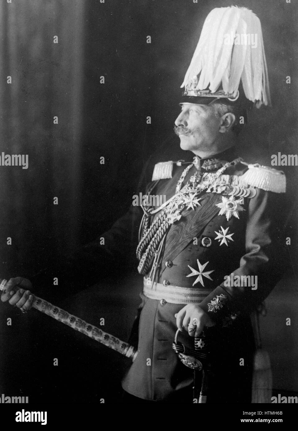 Wilhelm II, Imperatore Tedesco (Kaiser) dal 1888 al 1918. Tre quarti di lunghezza ritratto in piedi in uniforme militare rivolto verso sinistra, con casco piumati e tenendo un Maresciallo di Campo è testimone Foto Stock