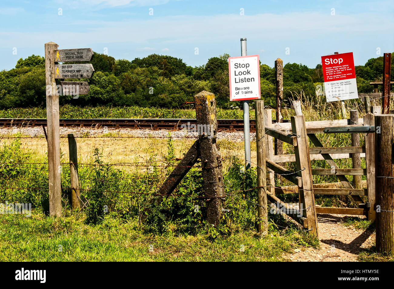 Un di legno gated attraversamento pedonale attraverso le linee ferroviarie totalmente complimentato con attenzione e segni di direzione nella calda sunkissed paesaggio inglese Foto Stock