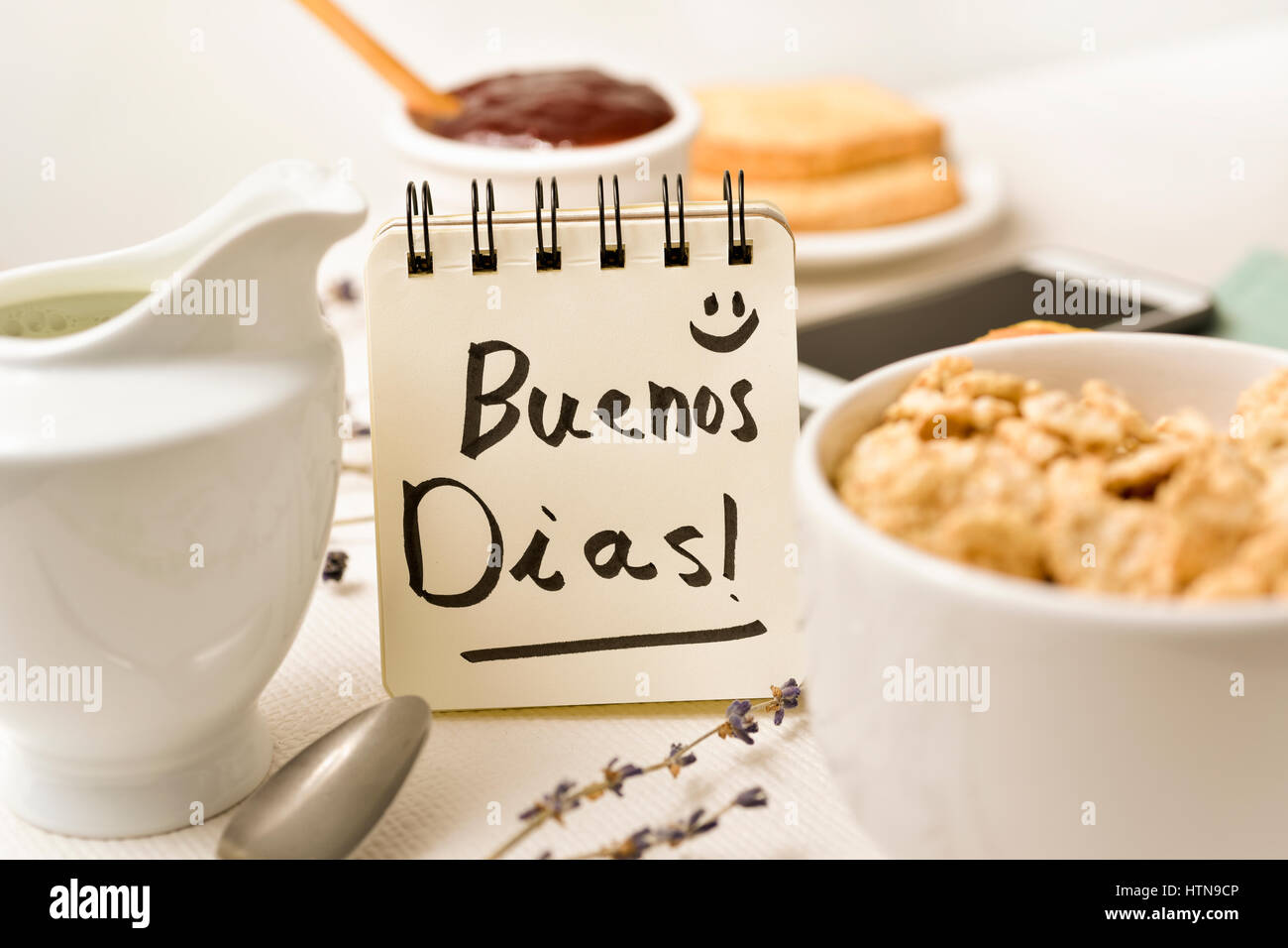 Primo piano di un tavolo per la prima colazione con un vaso di porcellana con cereali, qualche toast una ciotola con marmellata e una nota con il testo di buona mattina scritto in Foto Stock