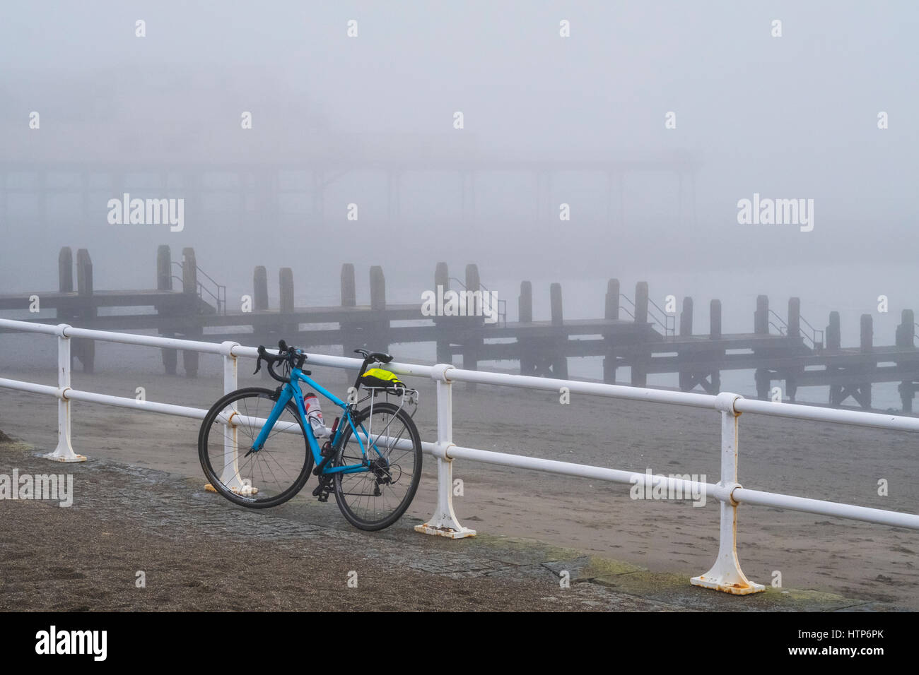 Aberystwyth, Wales, Regno Unito. Xiv Mar, 2017. La cittadina di mare è avvolto in una nebbia o mare-nebbia. n questa foto di un luminoso bicicletta cooured appoggia contro il lungomare di ringhiere, con un pontile in legno e pier in background. Credito: Alan Hale/Alamy Live News Foto Stock