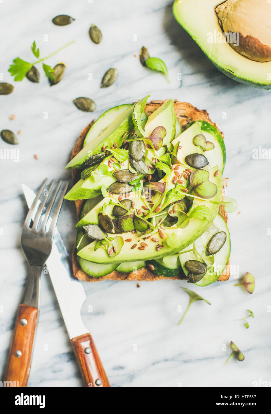 Verde sana colazione veggie concetto. Sandwich con avocado, cetriolo, kale, kress germogli di soia, i semi di zucca su sfondo marmo, vista dall'alto. Vegano w Foto Stock