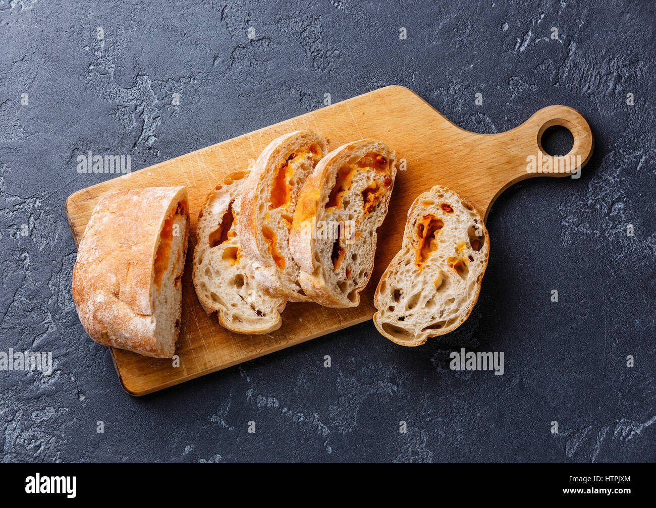 Fette di pane Ciabatta con formaggio sul bordo di taglio su sfondo scuro Foto Stock