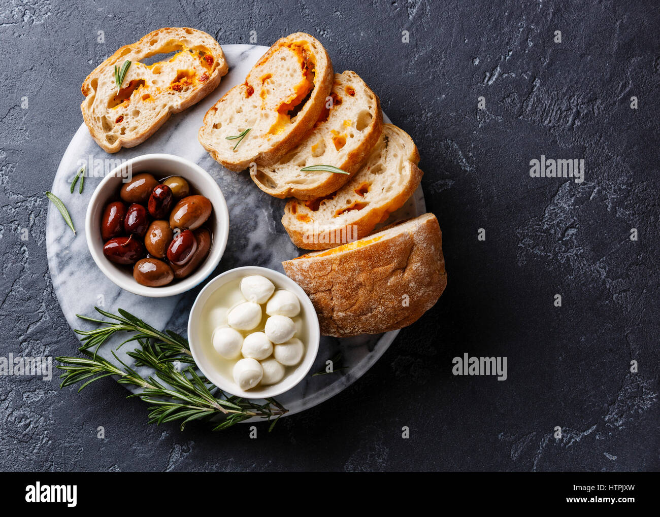 Olive, mini mozzarella tagliata a fette e Ciabatta pane con formaggio su sfondo scuro spazio copia Foto Stock