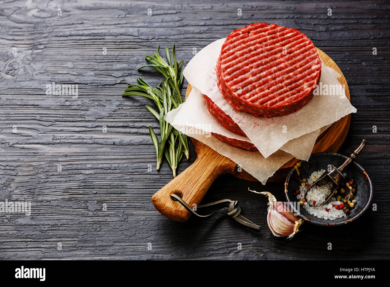 Materie di macinato di manzo hamburger di carne costolette di manzo e condimenti su nero di legno bruciato sfondo spazio di copia Foto Stock