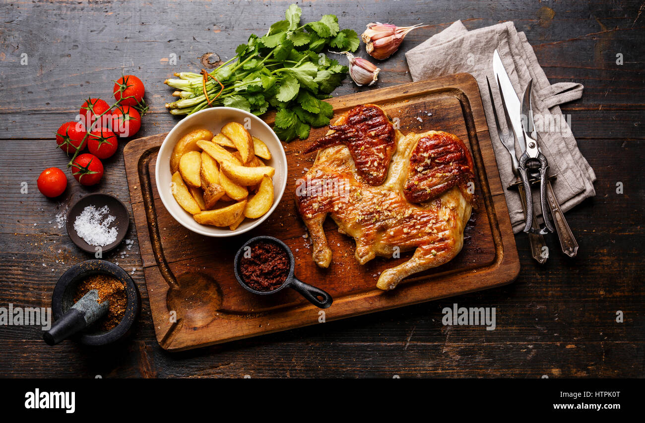 Grigliata di fritto di pollo arrosto Tabaka e Spicchi di patate sul bordo di taglio su sfondo di legno Foto Stock